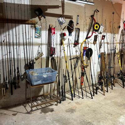 Sale Photo Thumbnail #40: Large collection of vintage and modern fishing rods, reels, and tackle displayed against a garage wall alongside assorted hand tools and a rolling cart.