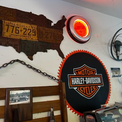 Sale Photo Thumbnail #94: Collection of automotive memorabilia, featuring a USA map made from vintage license plates, an illuminated Harley-Davidson neon clock, and a large sawblade-style Harley-Davidson sign.
