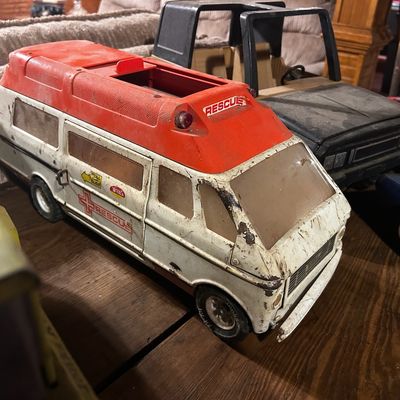 Sale Photo Thumbnail #124: Vintage Tonka pressed steel Rescue van vehicle, showing played-with condition with dirt and scuffing, alongside other vintage toy trucks on a wooden table.