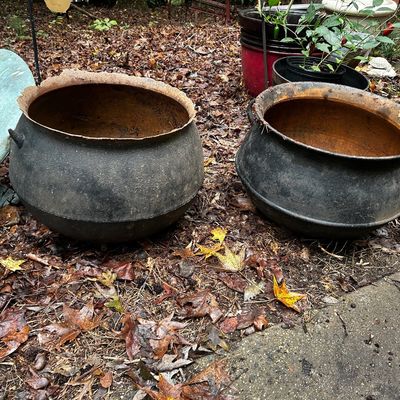 Sale Photo Thumbnail #122: Pair of antique cast iron cauldrons with heavy rusting on the interiors and rims, sitting outdoors alongside a weathered copper dolphin weather vane.