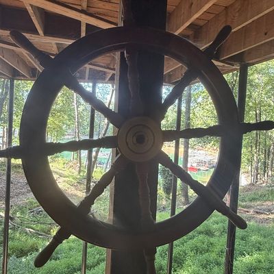 Sale Photo Thumbnail #229: Large vintage wooden ship's wheel mounted on a support beam, featuring eight turned spokes and a central brass hub.