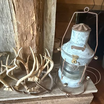 Sale Photo Thumbnail #245: Vintage galvanized metal maritime ship's lantern alongside a collection of natural deer antlers, displayed on a rustic wooden plank.