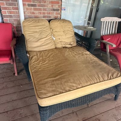 Sale Photo Thumbnail #227: Double outdoor wicker chaise lounge with tan cushions showing notable wear and dirt, set on a wooden deck next to red patio chairs.