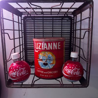 Sale Photo Thumbnail #101: Vintage metal wire crate displaying a red Luzianne coffee and chicory tin flanked by two Coca-Cola Christmas ornament bottles.