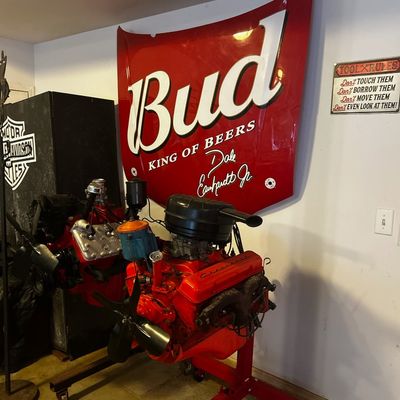 Sale Photo Thumbnail #46: Vintage Chevrolet V8 engines mounted on engine stands, set in front of a wall featuring a large Dale Earnhardt Jr. Budweiser hood metal sign.
