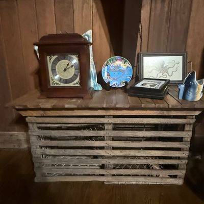 Sale Photo Thumbnail #246: Rustic wood slatted lobster trap table topped with a wooden mantle clock, decorative Florida Keys plate, framed octopus art, and ceramic shark vessel.