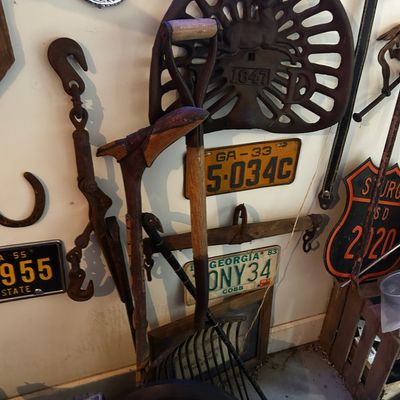 Sale Photo Thumbnail #95: Collection of vintage rustic decor items, including a cast iron tractor seat, old license plates, a shovel, pitchfork, carved walking stick, and heavy iron hooks.