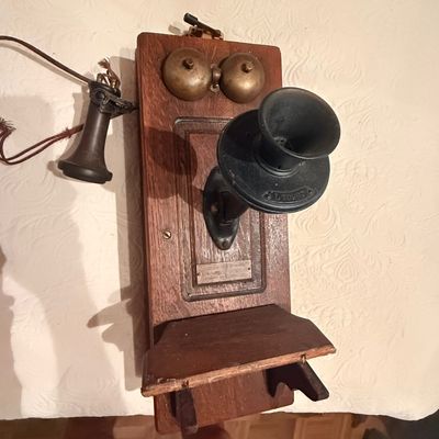 Sale Photo Thumbnail #221: Antique wooden wall-mounted crank telephone featuring brass bells, a black mouthpiece, and an attached earpiece.
