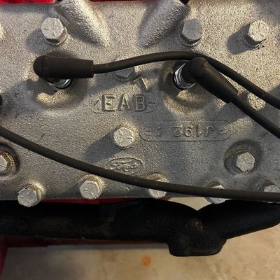 Sale Photo Thumbnail #54: Vintage Ford EAB flathead V8 cylinder head featuring raised casting marks, bolts, and spark plug wires.