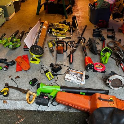 Sale Photo Thumbnail #41: Collection of power tools and lawn equipment including Ryobi leaf blowers, chainsaws, string trimmers, drills, and Yeti coolers arranged on a garage floor.