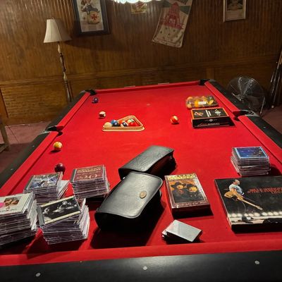 Sale Photo Thumbnail #183: Red felt billiard table displaying assorted music CDs, leather storage cases, and pool balls in a wood-paneled game room.