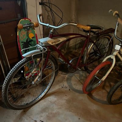 Sale Photo Thumbnail #127: Vintage red Schwinn cruiser bicycle alongside a white BMX bike and a vintage tropical graphic skateboard in a garage.