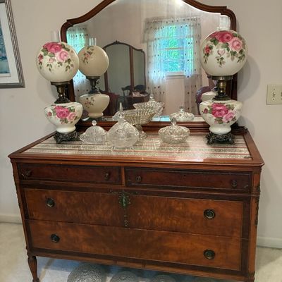 Sale Photo Thumbnail #213: Antique wood dresser with an arched mirror frame, displayed with a pair of floral painted hurricane lamps and pressed glass candy dishes.