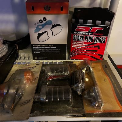 Sale Photo Thumbnail #5: Collection of boxed and packaged motorcycle parts and accessories, including Harley-Davidson fairing mount mirrors, Street Fire spark plug wires, turn signals, and foot pegs.