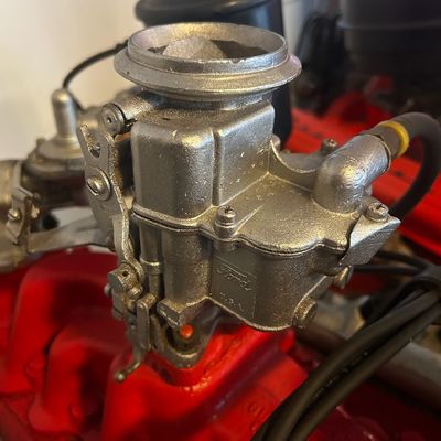Sale Photo Thumbnail #53: Vintage Ford cast-metal carburetor mounted on a red engine intake manifold.