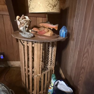 Sale Photo Thumbnail #247: Rustic wooden slat accent table featuring a fish-themed table lamp with a damask shade, surrounded by decor including a carved trout figurine, sea shells, and a large ceramic fish vase.
