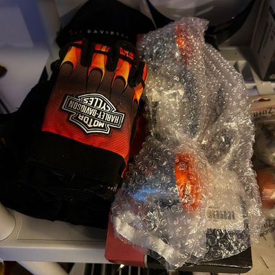 Sale Photo Thumbnail #6: Harley-Davidson flame print fingerless riding gloves resting next to bubble-wrapped motorcycle light assemblies on a shelf.
