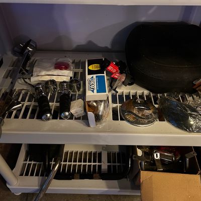 Sale Photo Thumbnail #7: Assortment of motorcycle parts and accessories on plastic shelving, including foot pegs, a seat cushion, Drag Specialties boxed items, and a chrome eagle medallion.