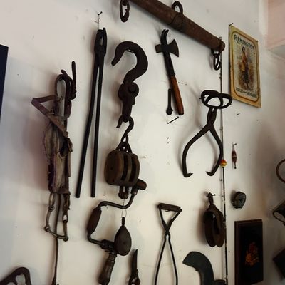 Sale Photo Thumbnail #158: Collection of rustic antique tools mounted on a wall, including iron tongs, a hand drill, a wooden single tree, and a vintage Remington advertisement sign.
