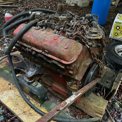 Sale Photo Thumbnail #112: Vintage V8 engine assembly featuring red valve covers, a carburetor, attached hoses, and heavy metal chains wrapped around the top.