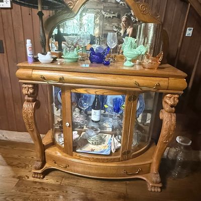 Sale Photo Thumbnail #249: Carved oak curio server featuring carved lion head legs, an attached arching mirror, and glass display doors housing various glassware.