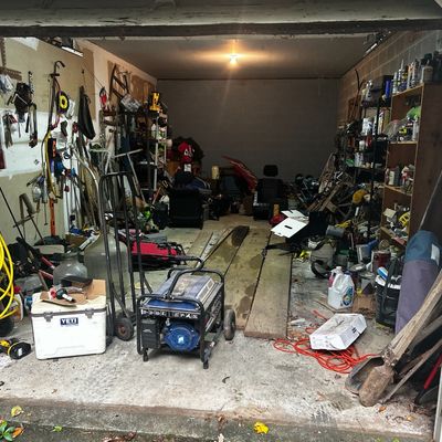 Sale Photo Thumbnail #59: Garage filled with various tools and equipment, including a portable generator, white Yeti cooler, hand trucks, air compressor hose, yard tools, and shelving units.