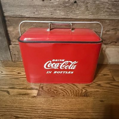 Sale Photo Thumbnail #237: Vintage red metal Coca-Cola picnic cooler with metal carrying handle and 'Drink Coca-Cola In Bottles' graphics.
