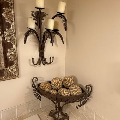 Sale Photo Thumbnail #234: Matching wrought iron palm frond candle sconce and pedestal bowl displaying decorative patterned orb fillers, set against a bathroom corner.