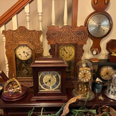 Sale Photo Thumbnail #182: Collection of vintage and antique clocks, including ornate pressed oak mantle clocks, brass anniversary clocks under glass domes, a barometer, and a brass telescope setup.