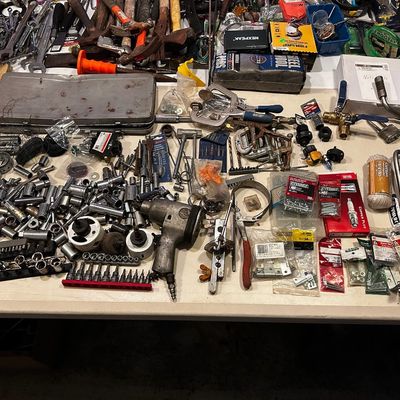 Sale Photo Thumbnail #3: Large assortment of hand and power tools, including socket sets, impact wrenches, clamps, hammers, and packaged hardware items arranged on a table.