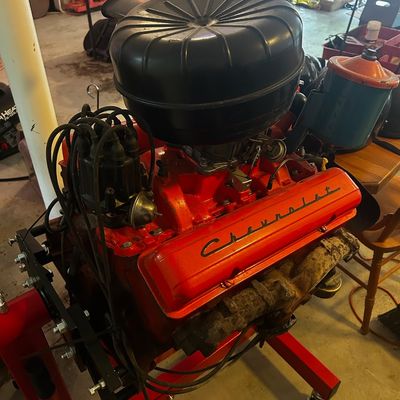 Sale Photo Thumbnail #47: Vintage Chevrolet V8 engine block mounted on a red rolling engine stand, featuring orange painted valve covers, script Chevrolet branding, and a black air cleaner.