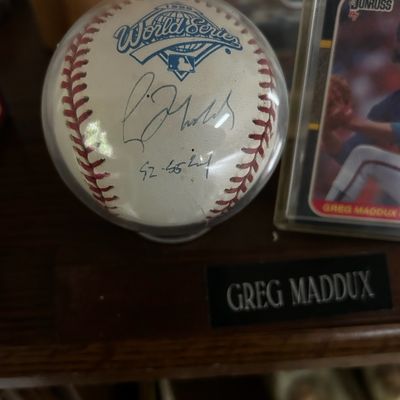 Sale Photo Thumbnail #64: Autographed 1995 World Series baseball signed by Greg Maddux, displayed in a clear protective cube next to a Donruss trading card.
