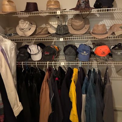 Sale Photo Thumbnail #202: Closet full of men's outerwear and hats, featuring various baseball caps, straw hats, fedoras, denim jackets, and winter coats.