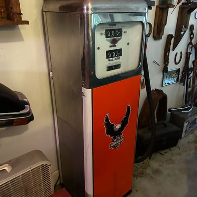 Sale Photo Thumbnail #93: Vintage orange and chrome gas pump adorned with a Harley-Davidson eagle decal, topped with a boxed 1955 Chevrolet Bel Air model car.