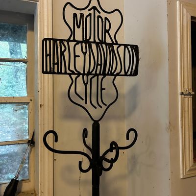 Sale Photo Thumbnail #106: Black wrought iron coat rack featuring a Harley-Davidson Motor Cycles shield logo topper with scrollwork hooks below.