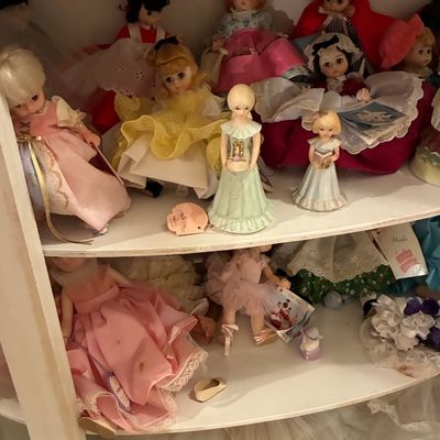 Sale Photo Thumbnail #205: Collection of vintage Madame Alexander and porcelain dolls in traditional dresses displayed on white shelving.