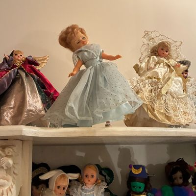Sale Photo Thumbnail #217: Collection of vintage storybook and character dolls displayed on white shelves, including Alexander-style dolls in formal gowns and costume attire.