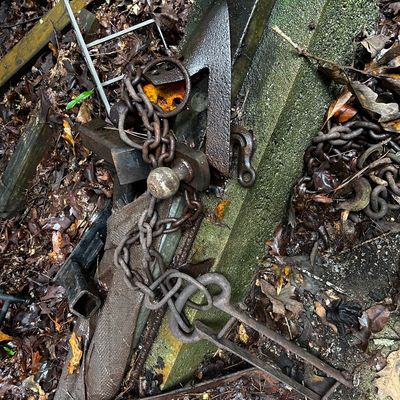 Sale Photo Thumbnail #116: Collection of rusted heavy-duty towing and agricultural equipment, including a trailer hitch ball, chains, hooks, and plow blades outdoor in leaves.