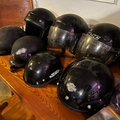 Sale Photo Thumbnail #25: Collection of black motorcycle helmets arranged on a wooden table, including full-face and half-shell styles from brands like HJC and Harley-Davidson.