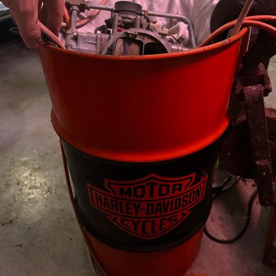 Sale Photo Thumbnail #104: Vintage Harley-Davidson orange and black metal oil drum containing mechanical engine parts.