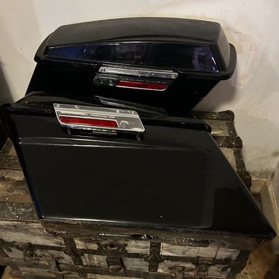 Sale Photo Thumbnail #23: Pair of glossy black Harley-Davidson motorcycle hard saddlebags with chrome latches, resting on a vintage trunk.