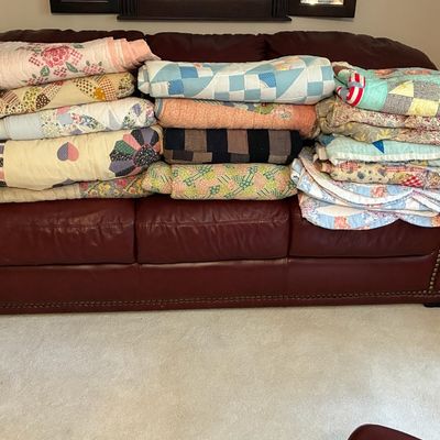 Sale Photo Thumbnail #209: Large collection of vintage handmade quilts with various patchwork patterns stacked on a burgundy leather sofa.