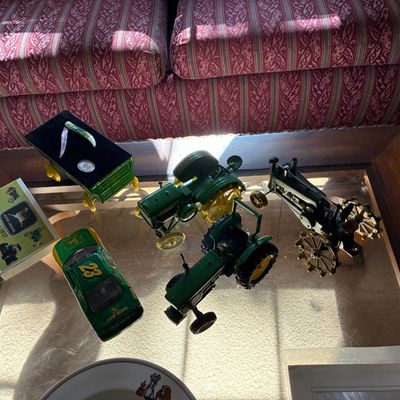 Sale Photo Thumbnail #197: Collection of John Deere collectibles including die-cast tractor models, a #23 race car, a miniature wagon, and commemorative stationery displayed on a glass-top table.