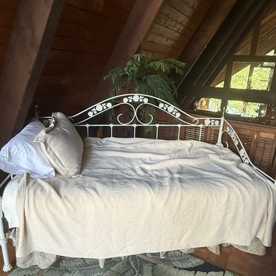 Sale Photo Thumbnail #239: White painted wrought iron daybed with floral scrollwork frame, made up with cream linens in an A-frame room.