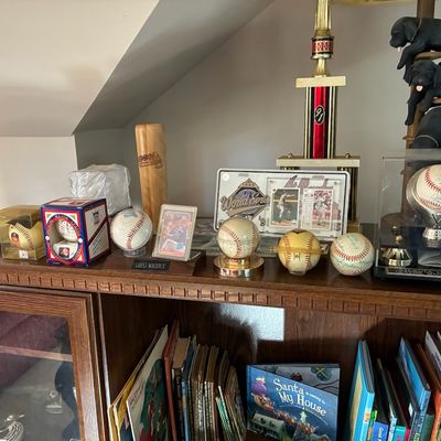 Sale Photo Thumbnail #198: Collection of Atlanta Braves baseball memorabilia display including autographed baseballs, trading cards, framed 1995 World Series commemorative plate, and a trophy.