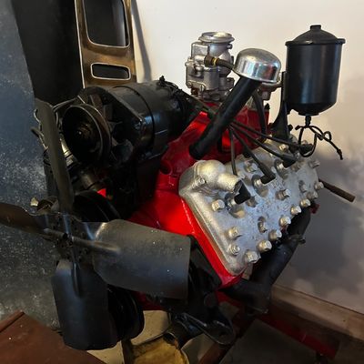 Sale Photo Thumbnail #109: Restored Ford Flathead V8 engine featuring a red painted block, silver cylinder heads, generator, carburetor, and fan assembly.