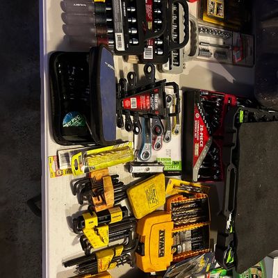 Sale Photo Thumbnail #22: Assortment of hand tools and drill bit sets, including Husky nut drivers, DeWalt bit cases, and various wrench sets arranged on a white folding table.