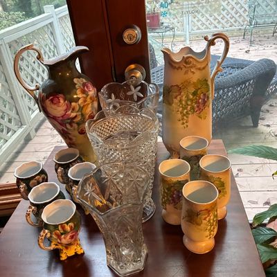 Sale Photo Thumbnail #178: Assortment of antique hand-painted porcelain ewes, matching mugs, and cut crystal glass vases displayed on a wooden table.