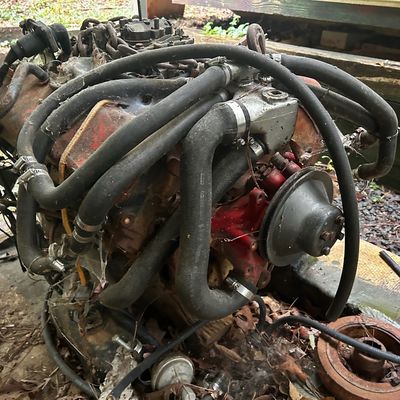 Sale Photo Thumbnail #113: Vintage V8 engine assembly showing surface rust, attached hoses, and red painted block components.