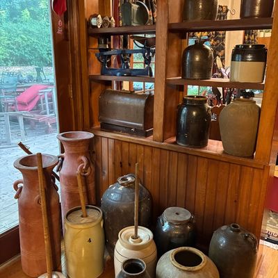 Sale Photo Thumbnail #175: Collection of rustic antique stoneware jugs, crocks, butter churns, and vintage scales displayed on wood shelving.